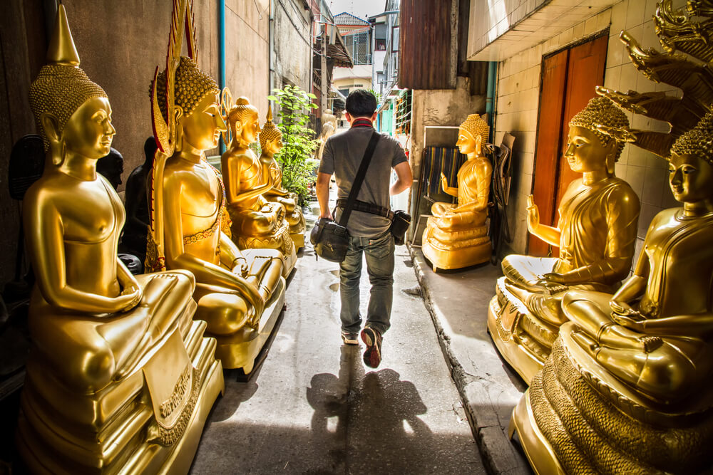 man walking through a hall of Buddha statues