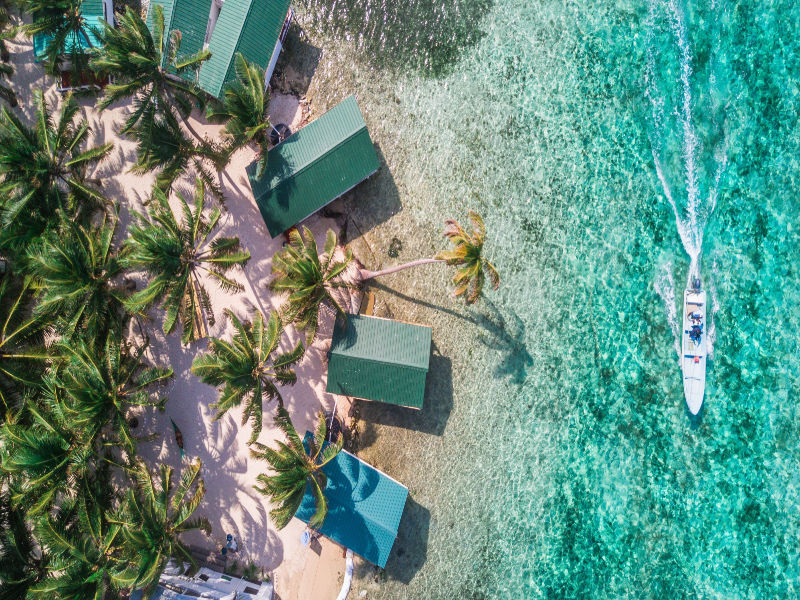 overhead shot of beach with green roofs and speedboat near th border of Belize and Guatemala