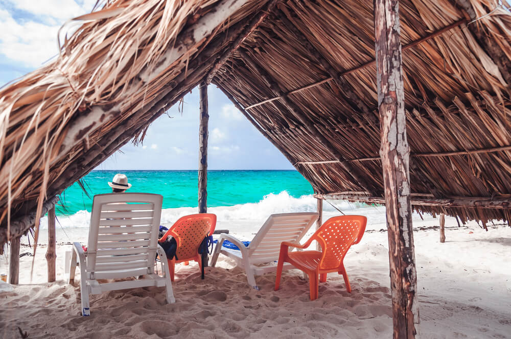 chairs under a palapa in front of the ocean