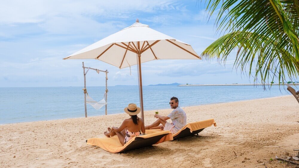 couple siting in loungers under an umbrella in Playa Arrocito, Mexico