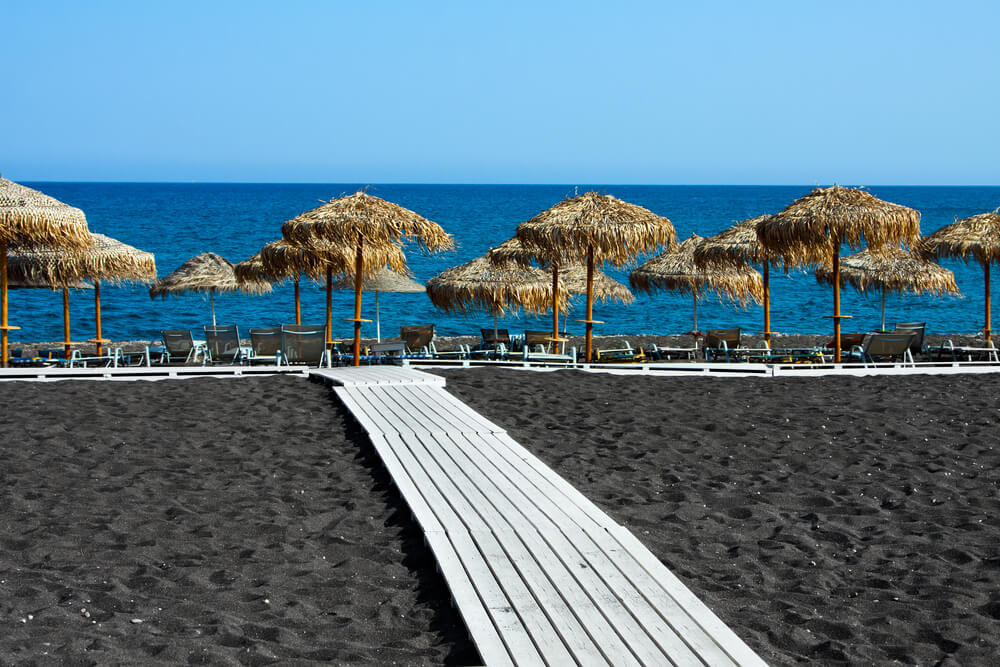white wooden walkway on black sandy Perivolos beach, Santorini