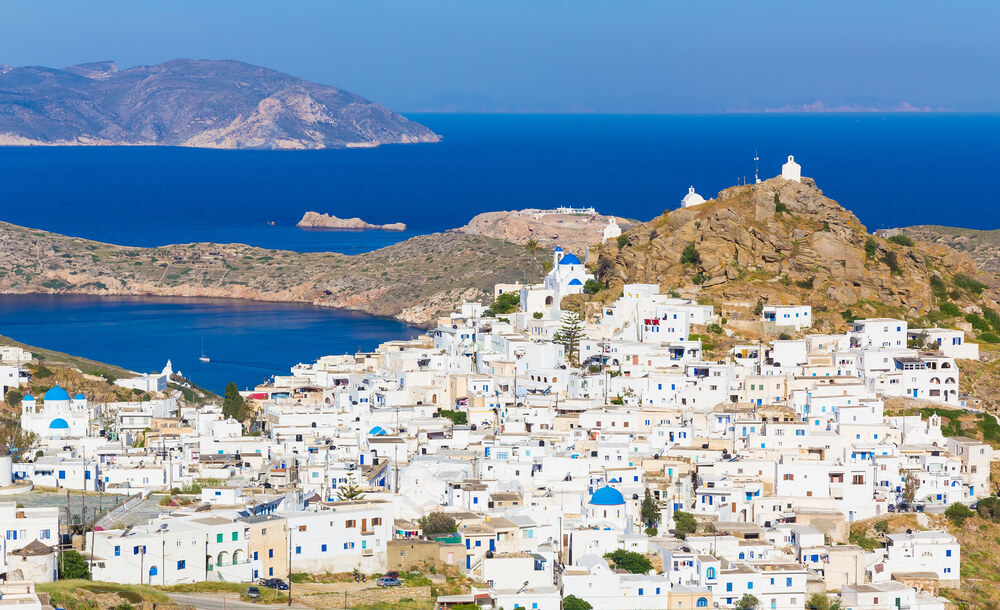 white village perched above a sapphire sea and craggy hills in the Greek islands