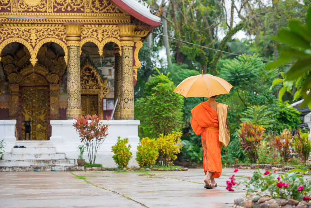 monk in orange robe by temple in Laos